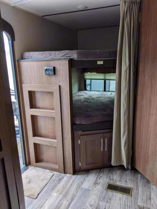 Inside an RV rental: two bunk beds with wood-look decor, a control panel, and privacy curtains.. Keystone RV Hideout Luxury 2021