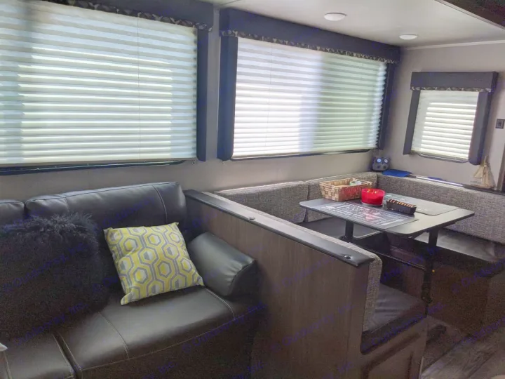 Inside a comfy RV rental: a spacious lounge with a black sofa and a U-shaped dining area for meals on the go.. Keystone RV Hideout Luxury 2021