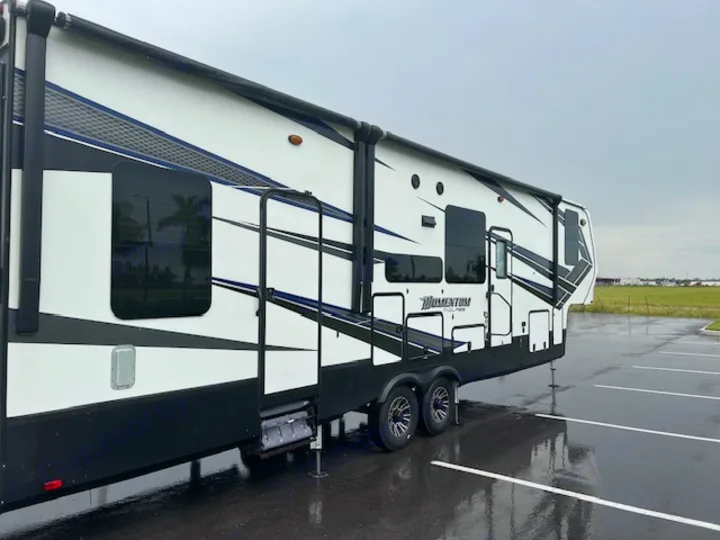 White and black RV rental, a modern Grand Design Momentum fifth wheel, parked on wet asphalt.. Grand Design Momentum 2018