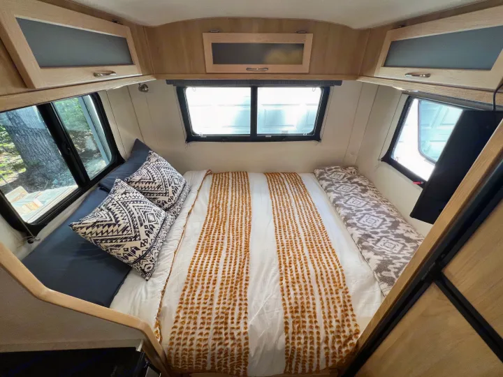 Discover this cozy RV rental's interior! A comfortable bed with patterned bedding, surrounded by windows & overhead storage.. Escape Trailer Escape Trailer Trailer 2022