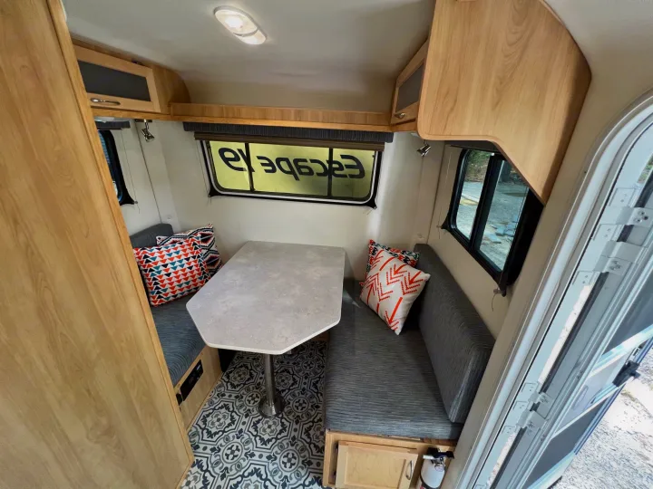 Explore this compact RV rental's interior, featuring a dining table, cozy benches, wood-look cabinets, and patterned floor.. Escape Trailer Escape Trailer Trailer 2022