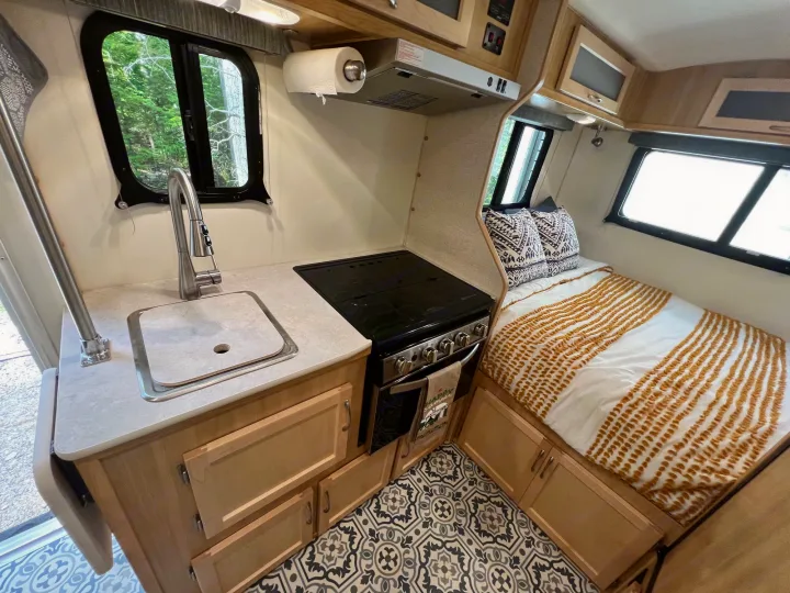 Explore this compact RV rental interior featuring a full kitchen, comfortable bed, and stylish patterned floor.. Escape Trailer Escape Trailer Trailer 2022