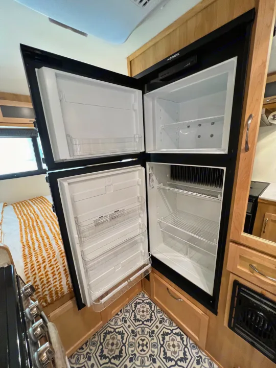Open Dometic RV rental refrigerator/freezer, revealing its empty shelves and door storage in the compact kitchen area.. Escape Trailer Escape Trailer Trailer 2022