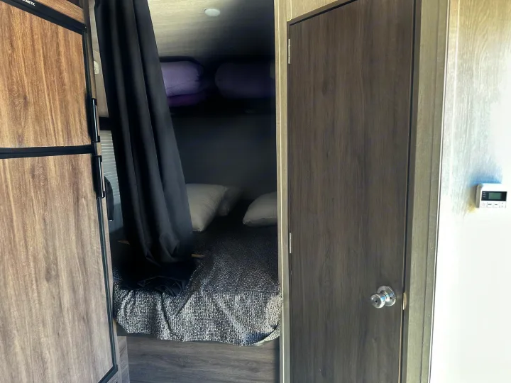 Inside an RV rental: bunk beds with a privacy curtain next to a refrigerator and a closed door with a thermostat.. Genesis Supreme Rv Powerlite Prime 1915 2022
