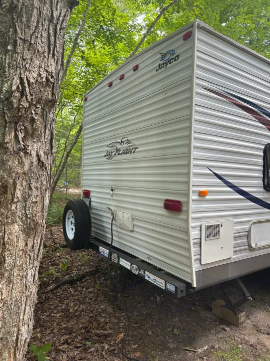 This RV rental is nestled in a lush, green campsite, showing its rear with a spare tire. Perfect for a nature escape.. Jayco Jay Flight 2009