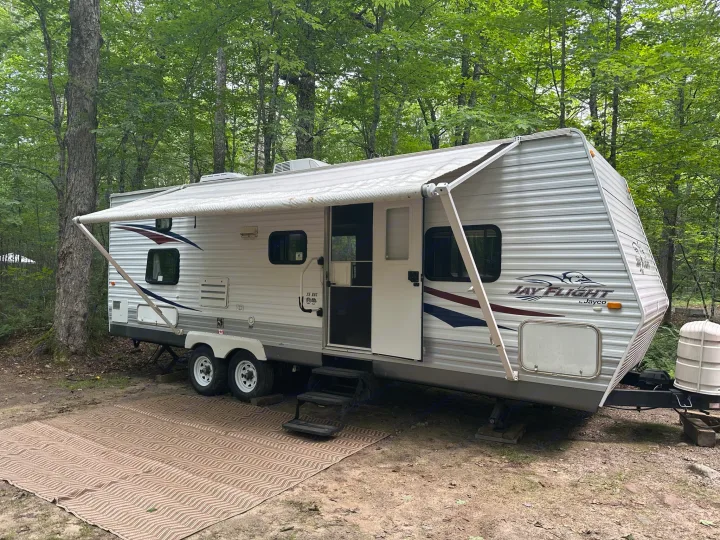 Spacious RV rental parked at a wooded campsite with awning extended. Perfect for outdoor adventures.. Jayco Jay Flight 2009