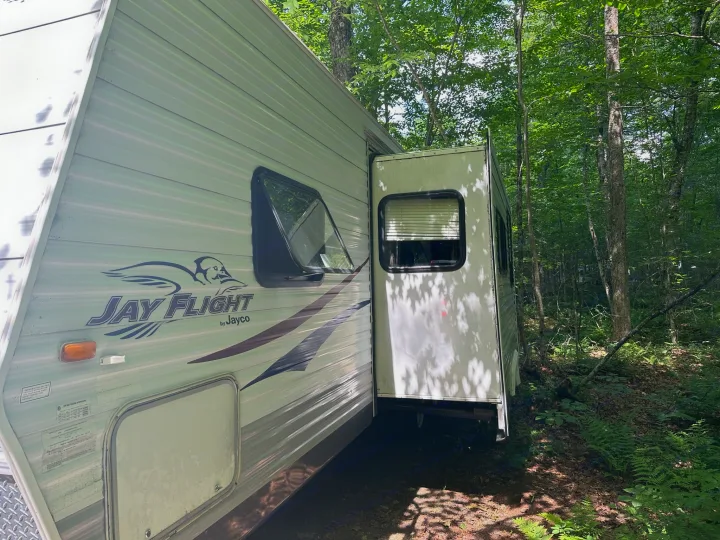 RV rental: A white Jay Flight travel trailer with a slide-out, parked in a sun-dappled, leafy forest. Ideal for nature trips.. Jayco Jay Flight 2009