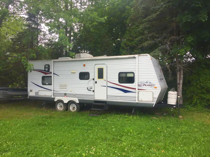 RV rental parked on grass amidst lush trees, with a boat nearby. Ideal for scenic camping trips and outdoor adventures.. Jayco Jay Flight 2009