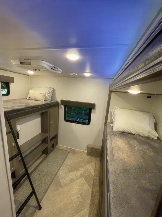 RV rental interior features a compact sleeping area with two bunk beds, ladder, AC, and a window.. East to West Alta 2021