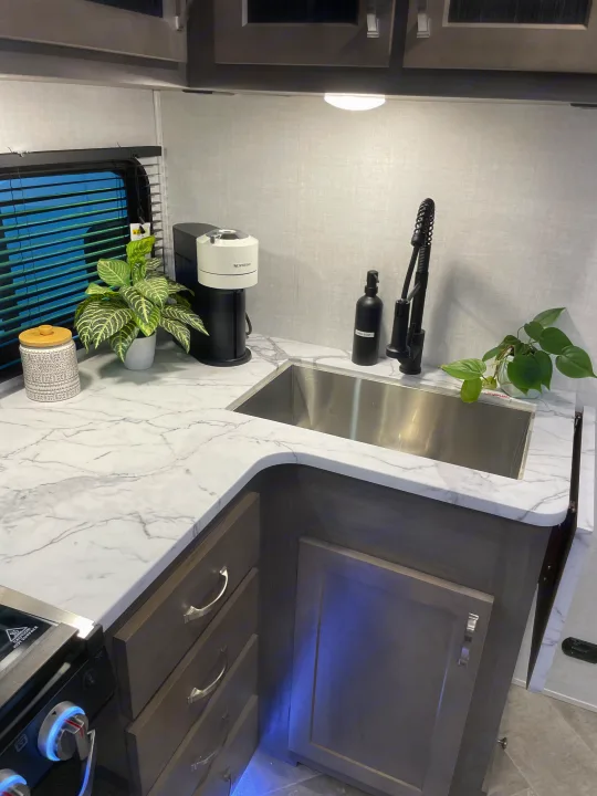 Modern RV rental kitchen with marble-look counters, sink, coffee maker, and plants. Functional and stylish.. East to West Alta 2021