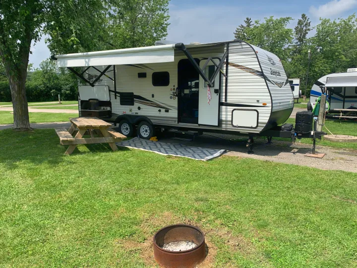 RV rental set up at a green campsite with a picnic table, awning extended, and fire pit in front.. Jayco Jay Flight SLX 2019