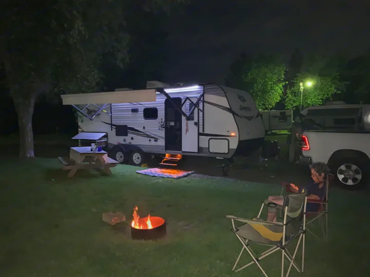 Night at a bright RV rental campsite: a person by a warm campfire near a travel trailer, with a pickup truck nearby.. Jayco Jay Flight SLX 2019