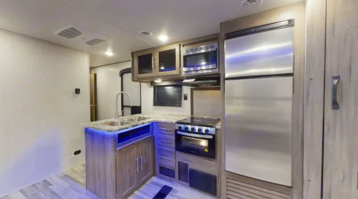 Modern compact kitchen in an RV rental, featuring stainless appliances, sink, and blue LED lighting, ideal for travel adventures.. Crossroads RV Zinger 2020