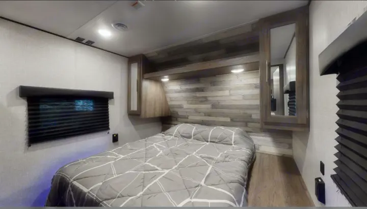 RV rental bedroom: a compact space with a grey bed, wood plank accent wall, overhead cabinets, and dark window blinds.. Crossroads RV Zinger 2020