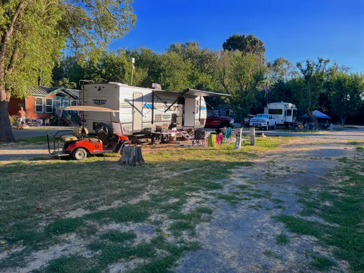 A sunny campground scene with a white travel trailer, red golf cart, and cabins. Ideal for an RV rental vacation.. Forest River Salem 2022