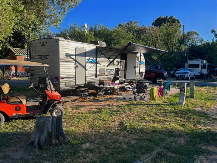 Bright day at an RV rental site: a modern travel trailer with awning, outdoor living area, and a red golf cart.. Forest River Salem 2022