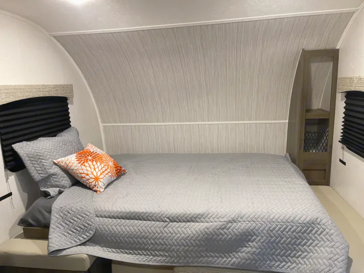 Inside an RV rental bedroom: A gray quilted bed, orange pillow, curved walls, and storage cabinet create a compact space.. Coachmen Viking 162RBU 2022