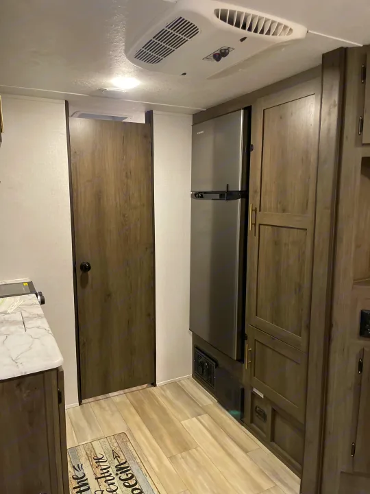 RV rental interior showing a stainless steel refrigerator, wood-look cabinets, ceiling AC unit, and light wood flooring.. Coachmen Viking 162RBU 2022