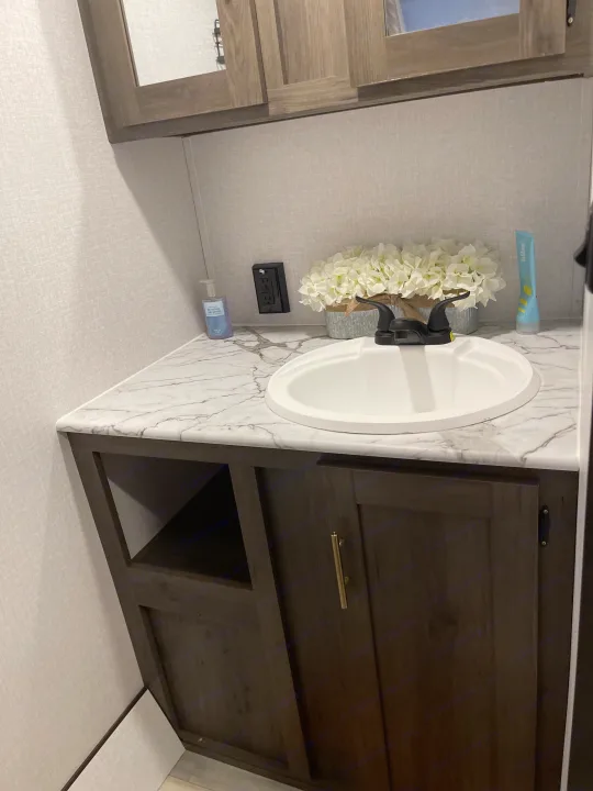 RV rental bathroom vanity with white sink, marble-look counter, dark wood cabinets, and decor, including flowers.. Coachmen Viking 162RBU 2022