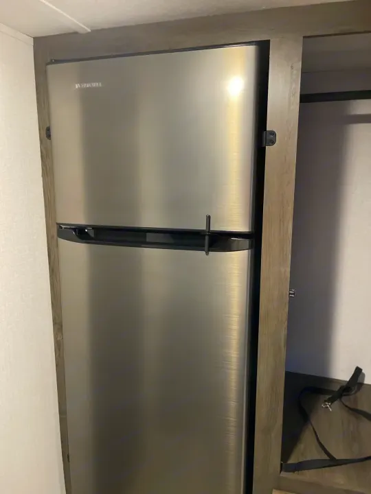 Stainless steel Everchill refrigerator with a safety latch in an rv rental, built into wooden cabinetry, next to open storage.. Coachmen Viking 162RBU 2022