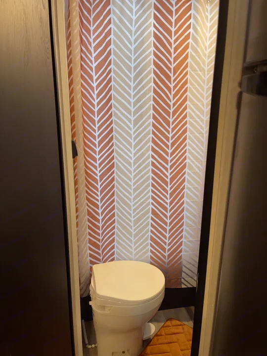 This compact RV rental bathroom features a white toilet and a stylish shower curtain with an orange and cream chevron pattern.. Coachmen Viking 162RBU 2022