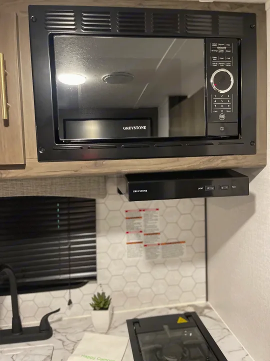 RV rental kitchen featuring a Greystone microwave, range hood, stovetop, and sink with a hexagonal tile backsplash.. Coachmen Viking 162RBU 2022