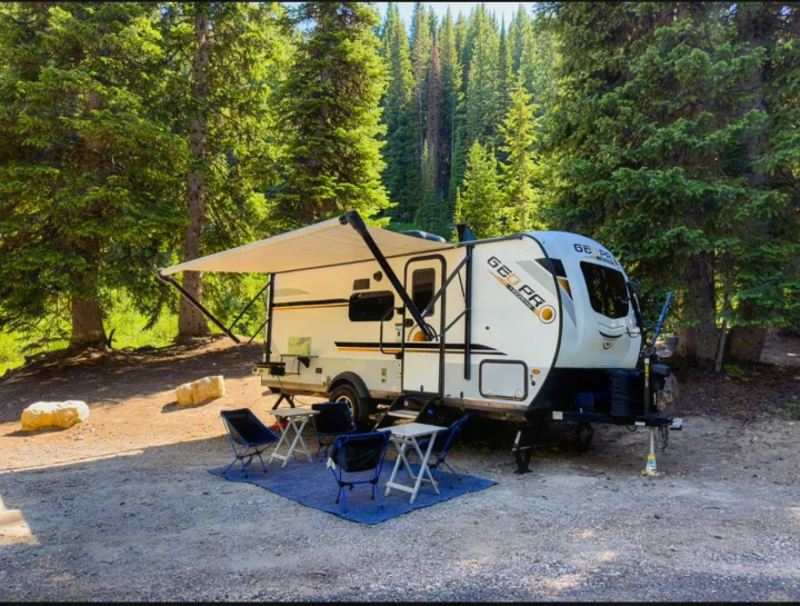 Relaxing Geo Pro rv rental campsite. Trailer with extended awning, outdoor chairs & tables, nestled among tall evergreen trees.. Forest River GeoPro 2021