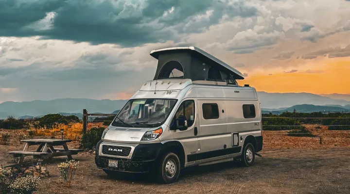 Silver camper van RV rental parked at a scenic mountain overlook. Dramatic sunset sky over mountains for a nature escape.. Winnebago Solis 2021