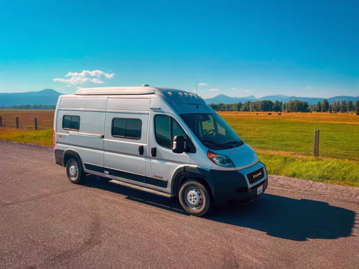 A silver Winnebago Solis RV rental van parked on a road, with mountains and green fields in the background.. Winnebago Solis 2021