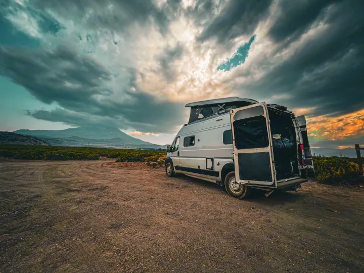 Experience outdoor travel with an RV rental! Modern pop-top camper van on a gravel road, mountains under dramatic skies.. Winnebago Solis 2021
