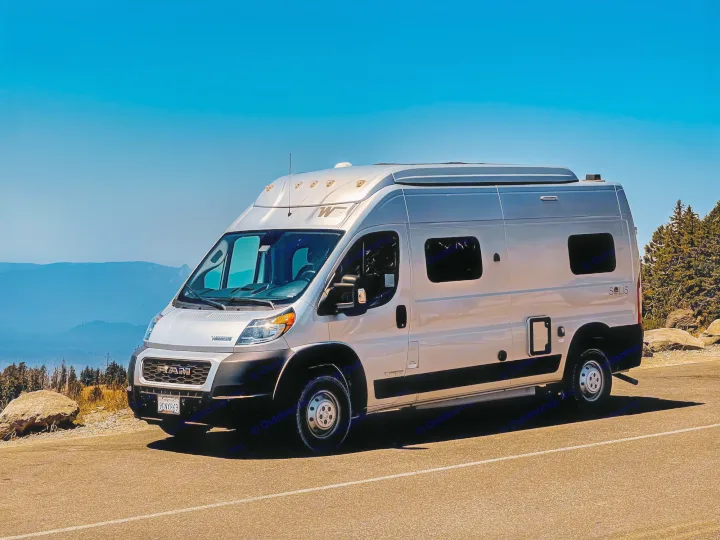 Silver RV rental camper van parked on a scenic mountain road under a clear blue sky, ready for adventure.. Winnebago Solis 2021