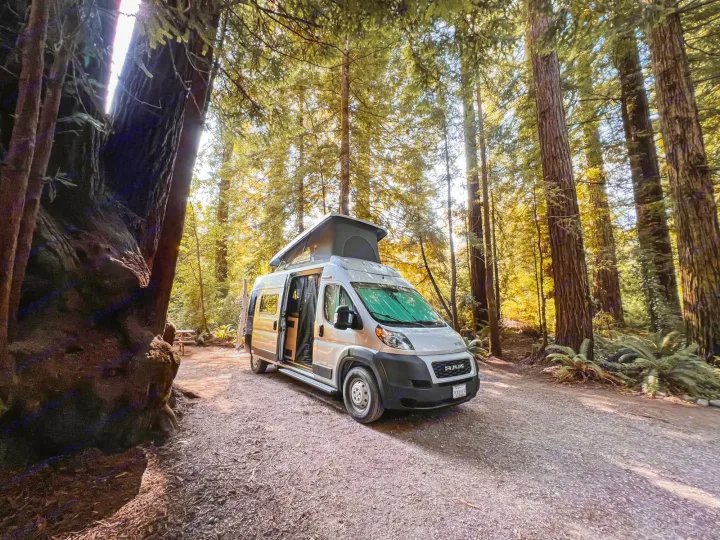 Sunlit RV rental camper van parked in a serene redwood forest campsite, ready for adventure.. Winnebago Solis 2021