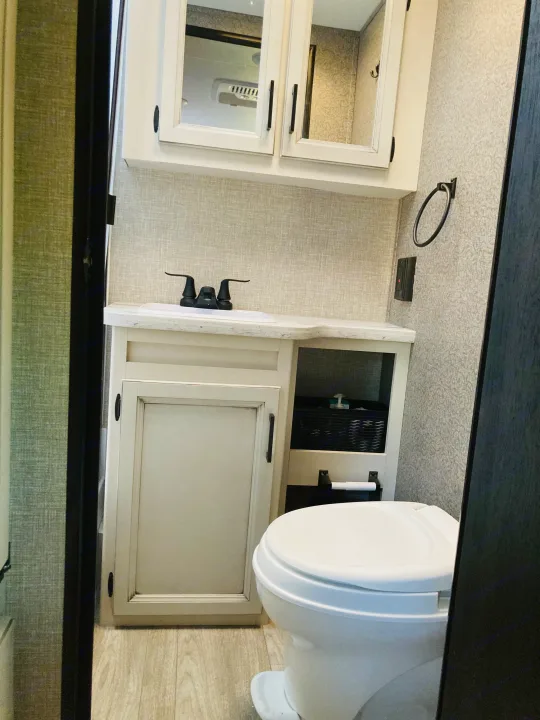 A bright, compact RV rental bathroom with a white sink vanity and medicine cabinet, next to a toilet and storage.. Jayco Jay Feather Micro 2022
