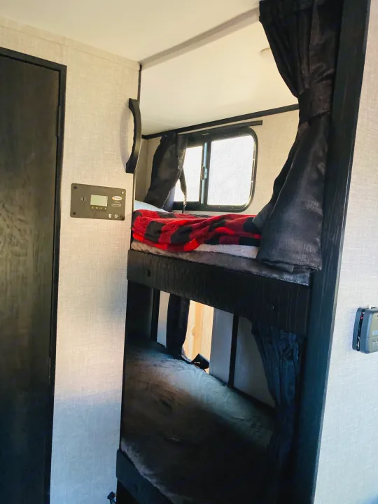 Inside an RV rental: a cozy bunk bed sleeping area with a window and control panel on the textured wall.. Jayco Jay Feather Micro 2022