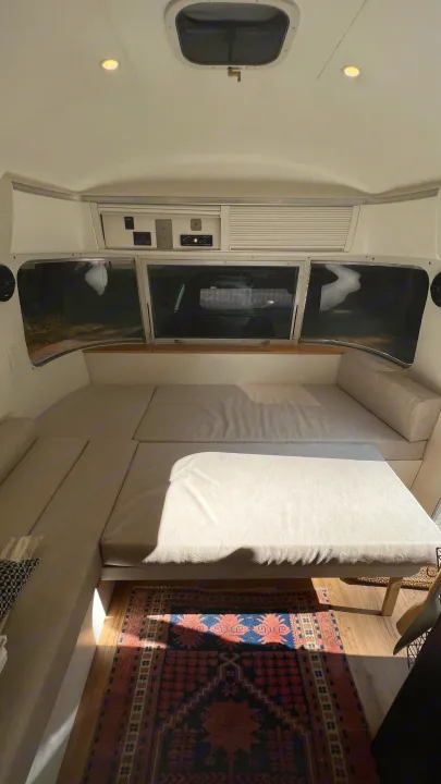 Inside this RV rental: light cushions create a convertible dinette/bed, featuring large windows, storage, and a cozy rug.. Airstream Argosy 1977