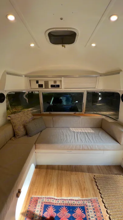 Spacious rv rental lounge with comfortable light-colored cushions, wood floor, and natural light from large windows.. Airstream Argosy 1977