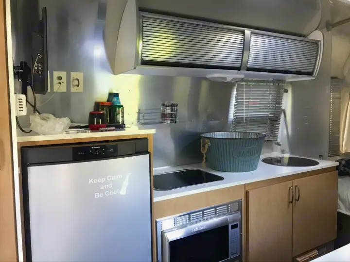 Compact RV rental kitchen featuring a fridge, microwave, sink, and sleek aluminum interior. Perfect for travel!. Airstream Sport 2012