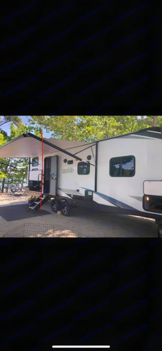 RV rental, a white and gray travel trailer, set up at a scenic lakeside campsite with its awning deployed.. Forest River Legend 2019