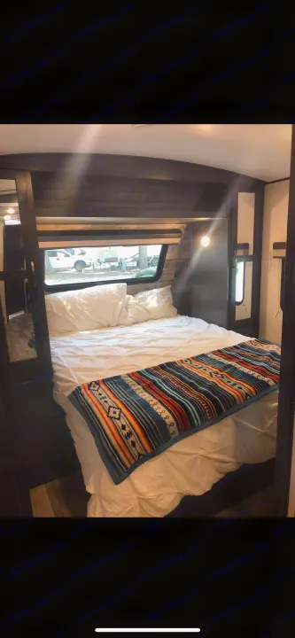 Cozy RV rental bedroom: full bed with white sheets, colorful patterned blanket, and a window view of outside.. Forest River Legend 2019