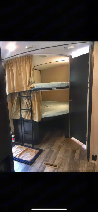 Compact RV rental: bunk beds with light sheets, a ladder, privacy curtains, and textured wood-look flooring.. Forest River Legend 2019