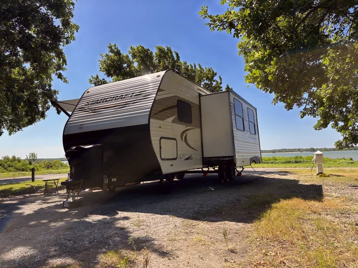 Starcraft RV rental enjoying a serene lakeside campsite with its slide-out extended, surrounded by trees and a blue sky, ideal for travel adventures.. Starcraft Autumn Ridge 2022