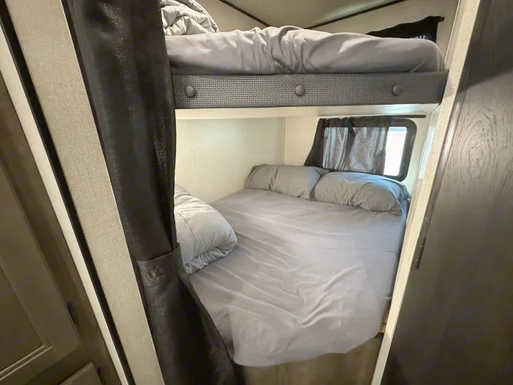 Cozy gray bunk beds in an RV rental, offering a comfortable sleeping area with curtains and windows.. Starcraft Autumn Ridge 2022