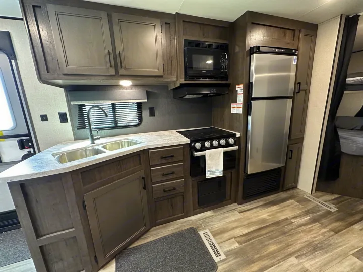 Inside an RV rental: a well-equipped kitchen featuring a sink, microwave, stove, & fridge, plus bunk beds.. Starcraft Autumn Ridge 2022