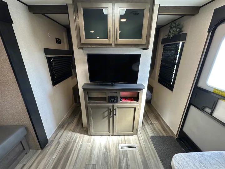 Inside this modern RV rental, a central TV and cabinets are flanked by hallways, windows with blinds, and an entry door.. Starcraft Autumn Ridge 2022
