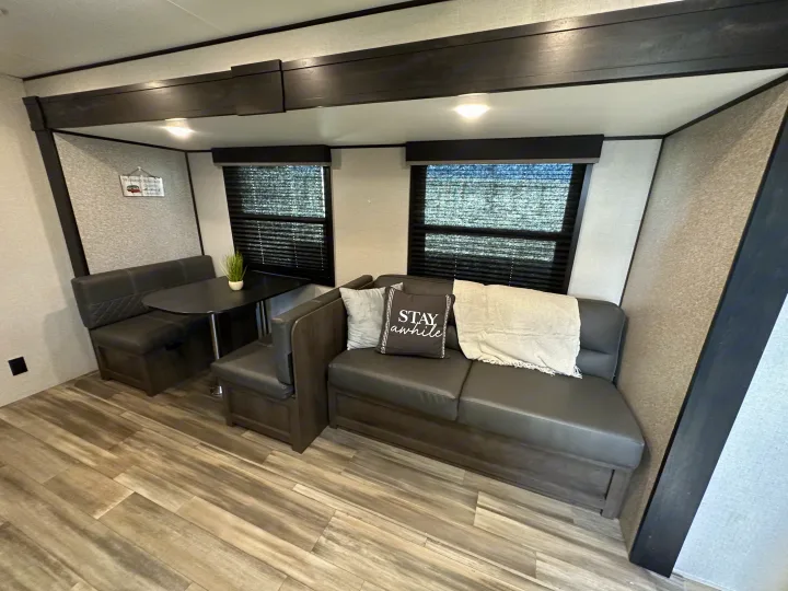 Cozy RV rental interior features a dining booth, sofa with 'STAY awhile' pillow, and wood flooring.. Starcraft Autumn Ridge 2022