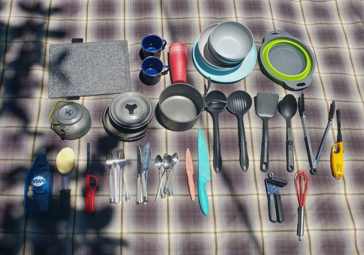 RV rental camping kitchen essentials: Cookware, dishes, utensils, and cleaning supplies laid out on a plaid blanket.. Nissan Xterra 2012