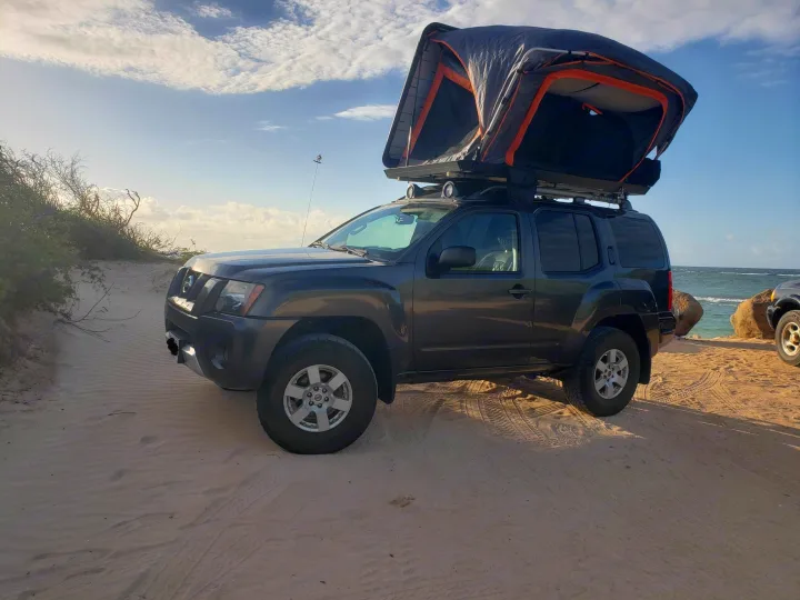 Dark gray Nissan Xterra SUV with a rooftop tent on a sandy beach, ideal for an rv rental off-road adventure.. Other Other 2015