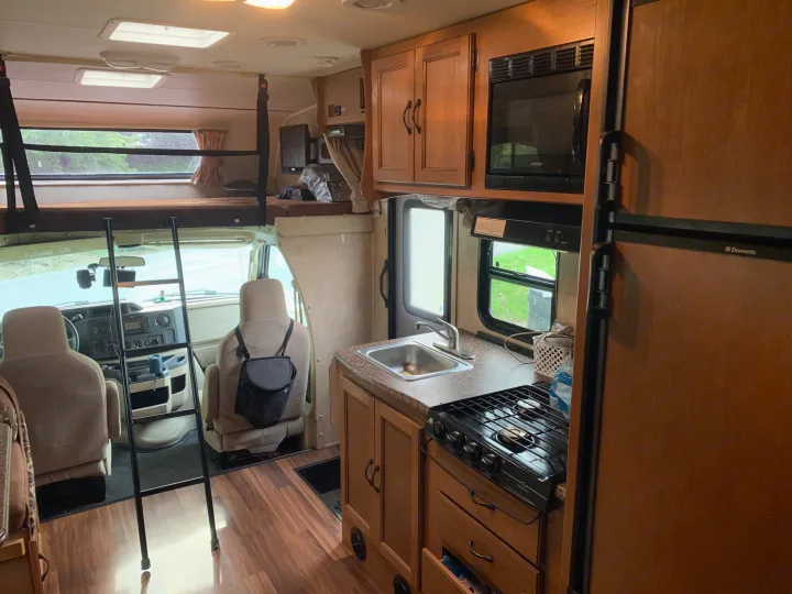 Cozy rv rental interior: front cab, over-cab bunk with ladder, and a full kitchenette including a stove, sink, & microwave.. Other Other 2014