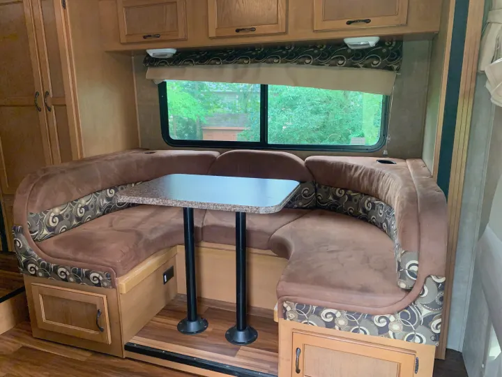 Cozy RV rental dinette with brown booth seating, a table, and large window overlooking trees, perfect for meals and relaxation.. Other Other 2014