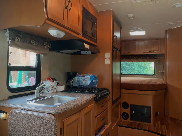 Spacious RV rental interior featuring a full kitchen with microwave, stove, sink, and refrigerator, plus a cozy bed area.. Other Other 2014